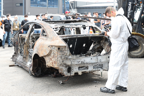 A Mercedes-Benz executive examines the burnt Mercedes EQE sedan in Incheon on Aug. 8. The Mercedes EQE EV explosion damaged as many as 880 vehicles parked in the garage. [NEWS1] 