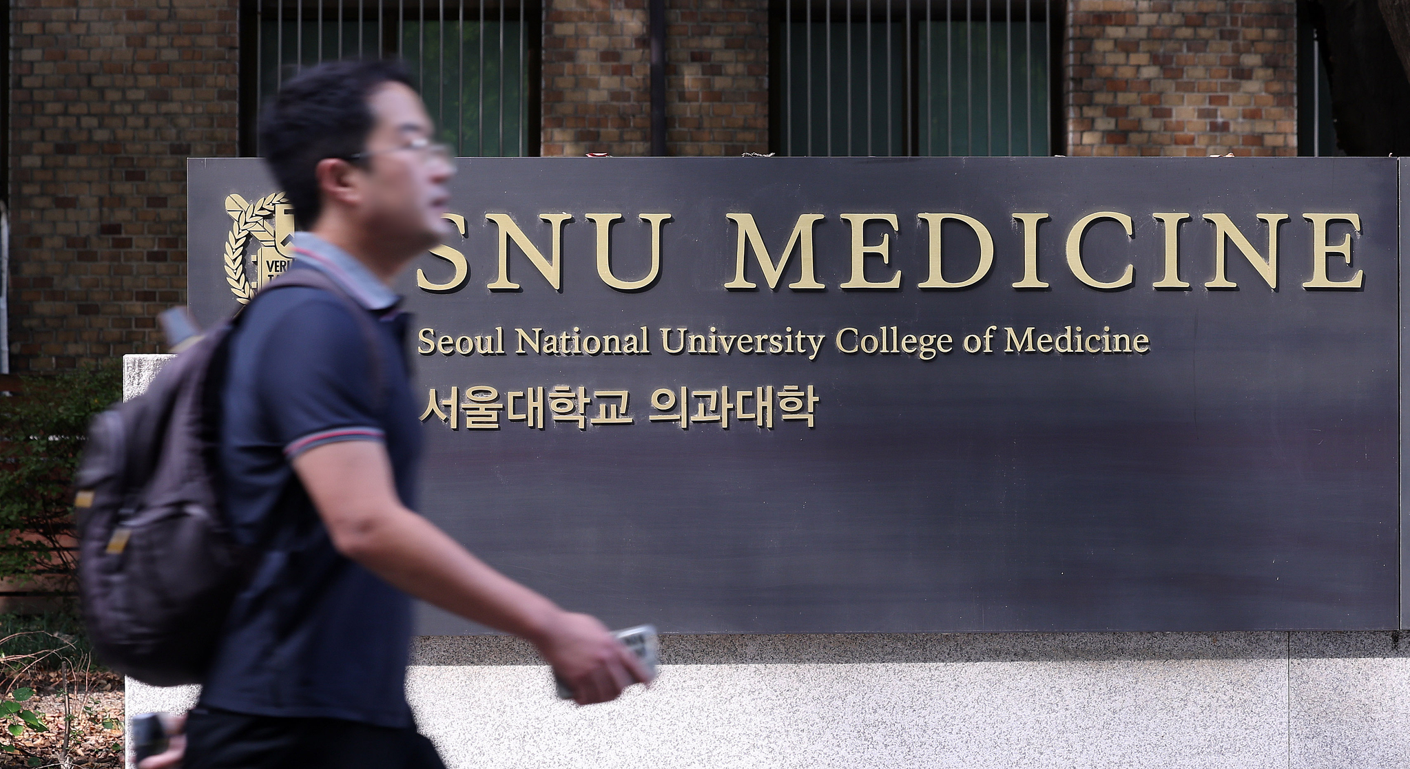 A pedestrian walks past the signboard of Seoul National University's College of Medicine in central Seoul on Monday, a day after the Ministry of Education conditionally allowed medical schools to process students' leave requests. [NEWS1] 