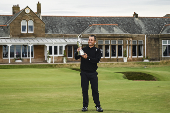 Xander Schauffele smiles with and looks at the Claret Jug trophy on the 18th hole green following his two stroke victory during the final round of The 152nd Open Championship at Royal Troon on July 21 in Troon, Scotland. [GETTY IMAGES]