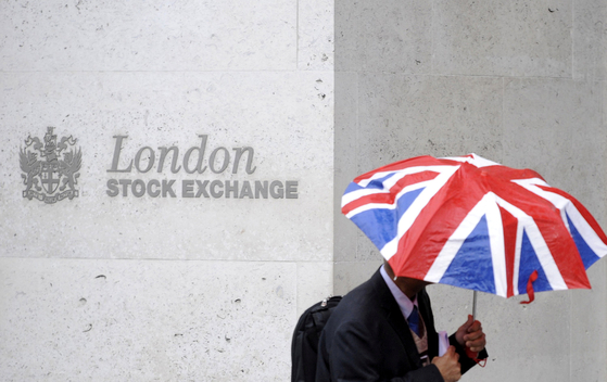 A worker shelters from the rain under a Union Flag umbrella as he passes the London Stock Exchange in London. [REUTERS]