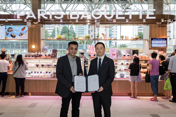 Paris Croissant CEO Hur Jin-soo, right, poses for the camera with Berjaya Food Director and CEO Dato’ Sydney Lawrance Quays after signing a master franchise agreement with the Kuala Lumpur-based food company at Paris Baguette's Parkway Parade branch in Singapore on Monday. [SPC GROUP]