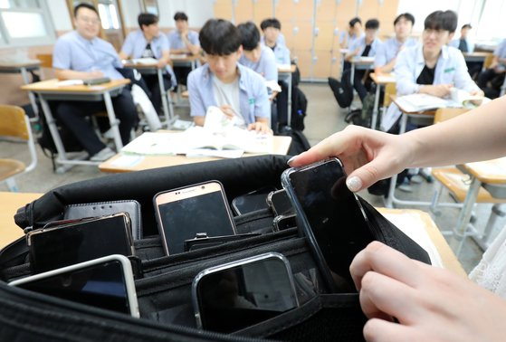 A teacher collects mobile phones in a first-year classroom at Dongsan High School in Daejeon in September last year. [NEWS1]