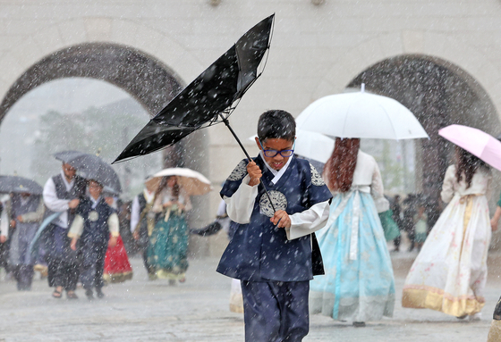 A child visiting Gyeongbokgung Palace in Jongno District, central Seoul, avoids rain with flipped umbrella on July 22. [NEWS1]