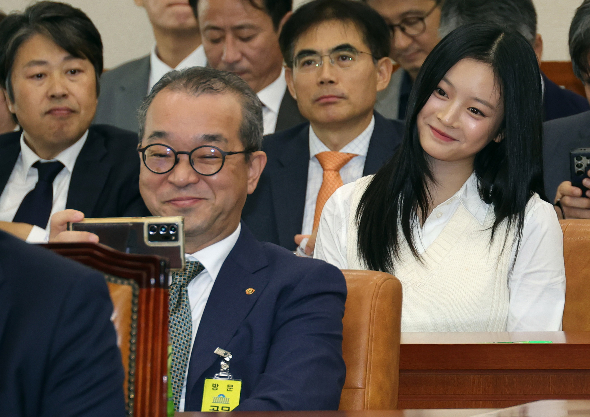 Jung In-sub, Hanwha Ocean’s head of Geoje shipyard, front, taking a selfie with NewJeans' Hanni while waiting to testify at a National Assembly audit in western Seoul on Oct. 15. [NEWS1]