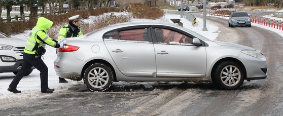 Police officers on Thursday help push a vehicle skidding on the road in Nohyeong-dong, Jeju. [NEWS1] 