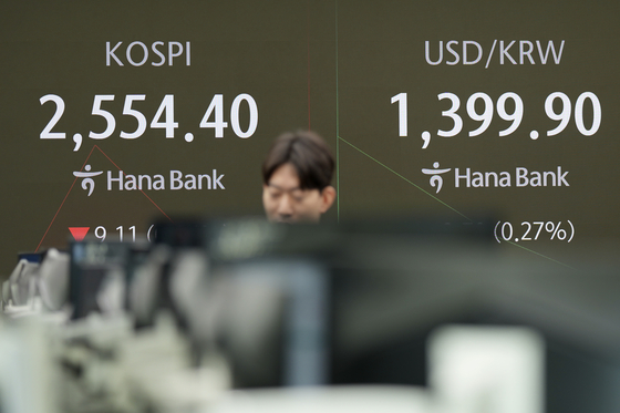 A currency trader walks by the screens showing the Kospi and the foreign exchange rate between the U.S. dollar and Korean won at a foreign exchange dealing room in Seoul on Thursday.  [AP/YONHAP]