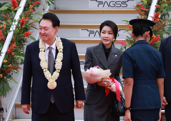 President Yoon Suk Yeol, left, and first lady Kim Keon Hee, center, smile as they are met with flowers at Ninoy Aquino International Airport in Manila on Oct. 6. [YONHAP]